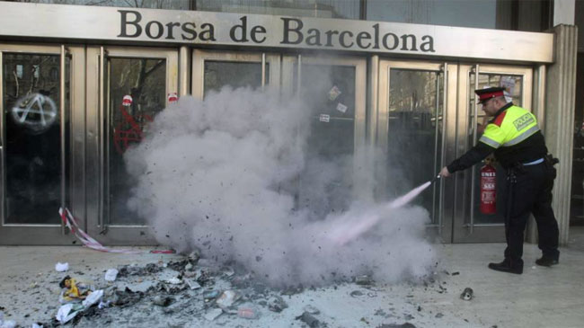 Un mosso apaga hoy el incendio provocado por un piquete de unas mil personas que protestaban frente a la Bolsa de Barcelona. | EFE/Alberto Estvez