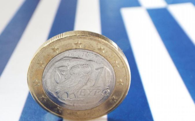 Imagen de una moneda de un euro sobre la bandera de Grecia