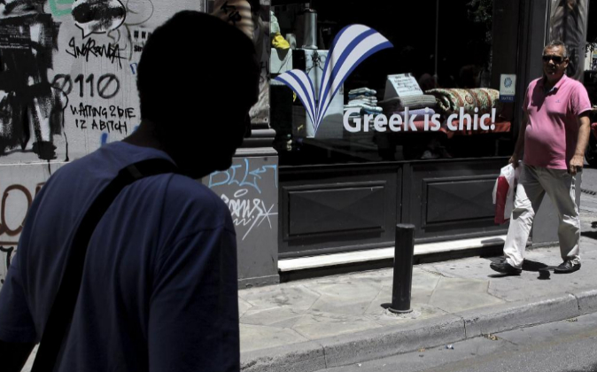 Viandantes pasan junto a un escaparate en Atenas, Grecia.