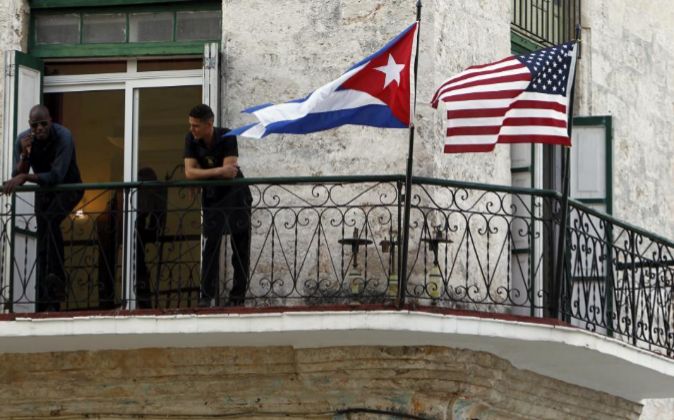 Dos jóvenes cubanos conversan junto a las banderas de Estados Unidos...