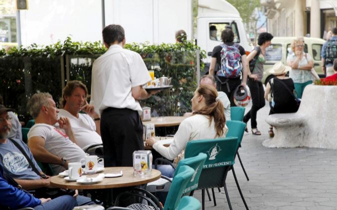 Un camarero sirve a unos turistas en una terraza en Barcelona.