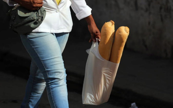 Una mujer camina con dos barras de pan en una bolsa de plástico.