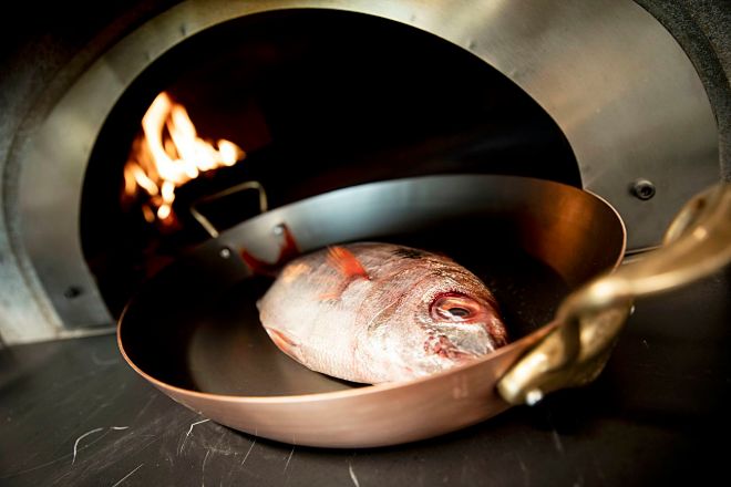 Besugo en la boca del horno de leña donde se cocinarán todos los pescados.