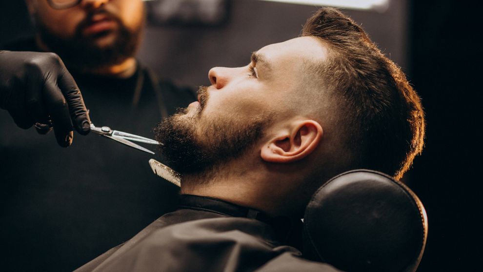 Un barbero profesional retoca la barba de un joven.