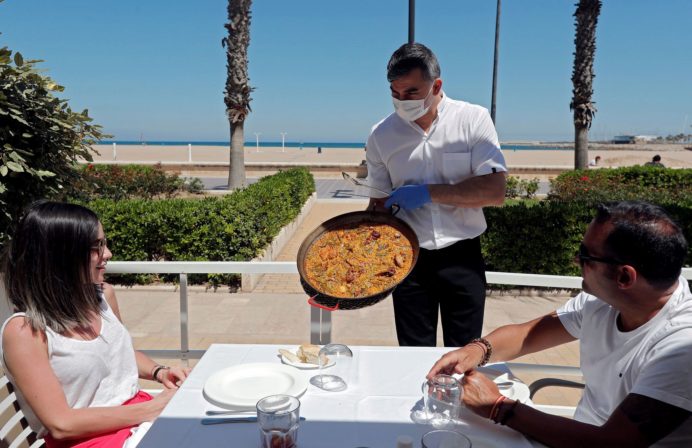 Un camarero sirve una paella en la terraza de un restaurante de la Playa de la Malvarrosa en Valencia.