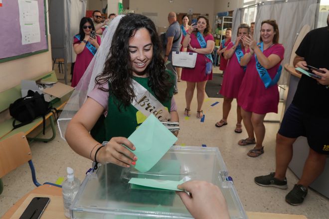 Una joven con velo y disfrazada para celebrar su despedida de soltera se dispone a introducir su papeleta de voto en una urna del IES La Caleta en el barrio de La Viña en Cádiz.