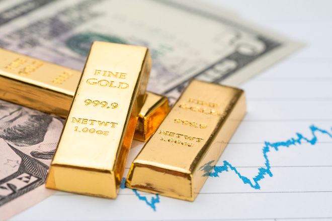 Lingotes de oro sobre billetes de dólar y gráficos de cotizaciones