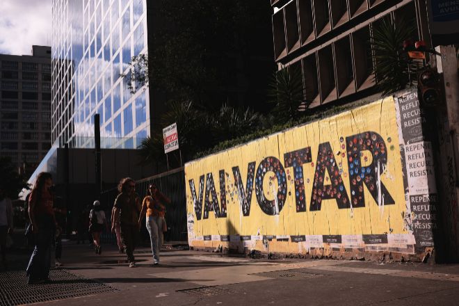 Varias personas caminan frente a un mural sobre las elecciones en Sao Paulo (Brasil).