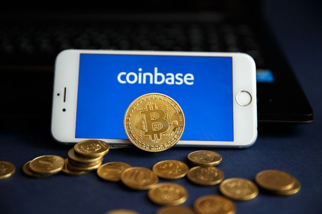 Aplicación de Coinbase en un móvil junto a monedas de bitcoin