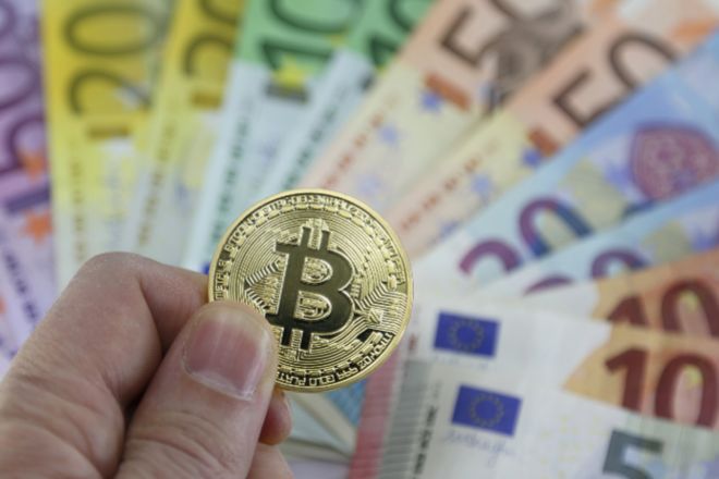 Moneda de bitcoin entre billetes de euro