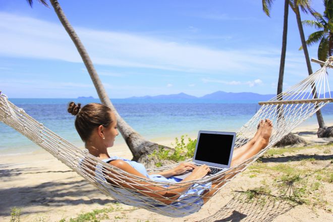 Mujer con un ordenador portatil, trabajando desde la playa.