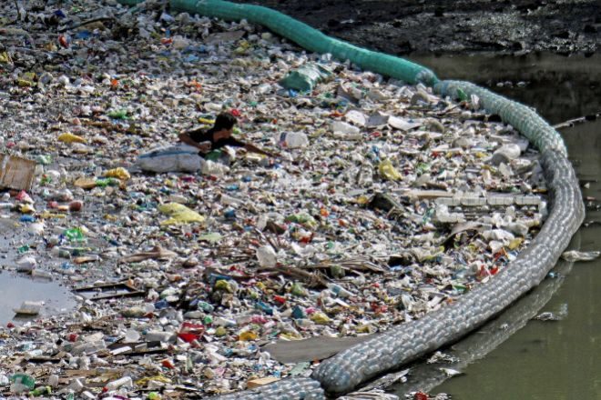 Un hombre recolecta botellas de plástico entre los residuos que una malla impide que alcancen el mar en un río en Cebu (Filipinas) en una imagen de archivo de 2019.